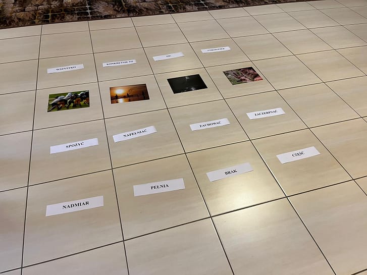Beige tiled floor with four small photos and Polish phrases on white cards laid out like a grid.